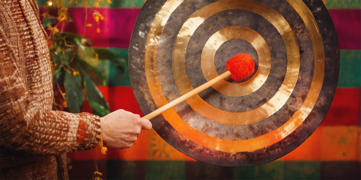 Person striking a spiral designed gong with a red mallet